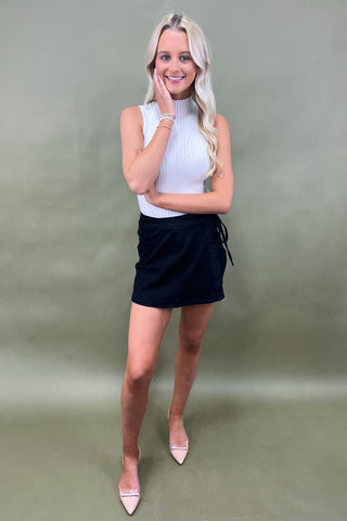 Woman wearing a white top and black skirt against a plain background