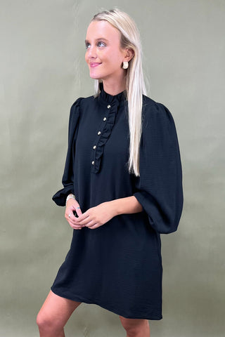 Woman wearing a black dress with ruffled details against a plain background