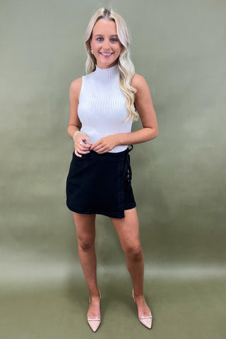 Woman wearing a white sleeveless top and black skirt against a green background