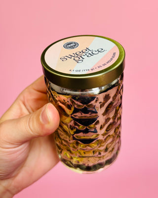 Hand holding a jar labeled 'sweet grace' against a pink background