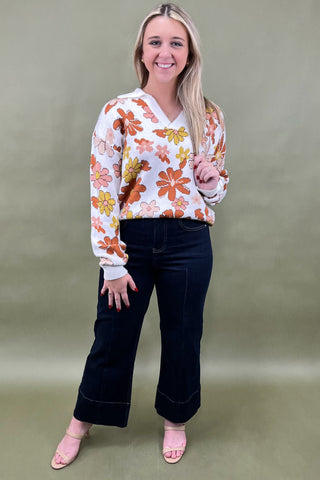 Woman wearing a floral sweater and black pants against a green background