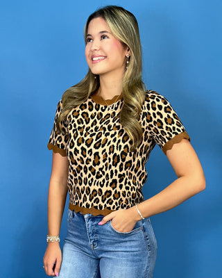 A woman wearing a short-sleeve leopard print top with brown trim, paired with blue jeans