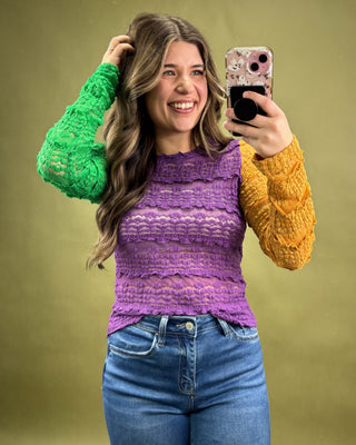 Woman taking a selfie with a phone, wearing a colorful sweater and jeans on a green background