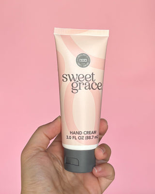 Hand holding a tube of sweet grace hand cream against a pink background