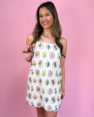 Woman wearing a white dress with colorful patterns against a pink background