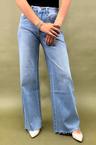 Person wearing light blue flared jeans on a green background