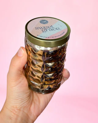 Hand holding a jar labeled 'sweet grace' against a pink background