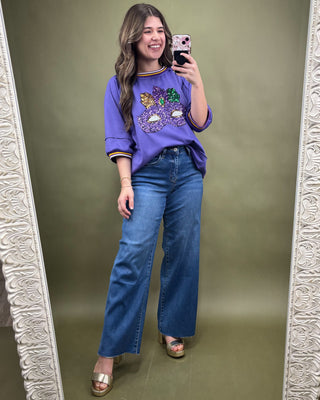 Woman taking a mirror selfie wearing a purple sweater with a graphic design and blue jeans.