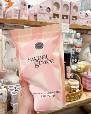 Hand holding a 'sweet grace' mineral soaking salts package in a store setting.