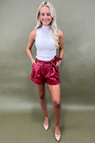 Woman wearing a white top and red shorts against a plain background