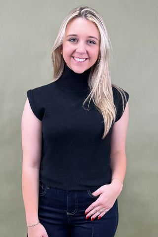 Woman wearing a black sleeveless turtleneck top against a plain background