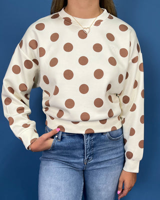 A person wearing a cream sweatshirt with large brown polka dots, paired with blue jeans