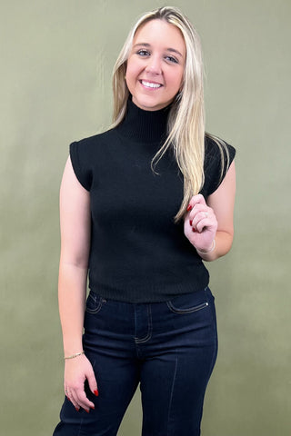 Woman wearing a black sleeveless turtleneck top against a green background