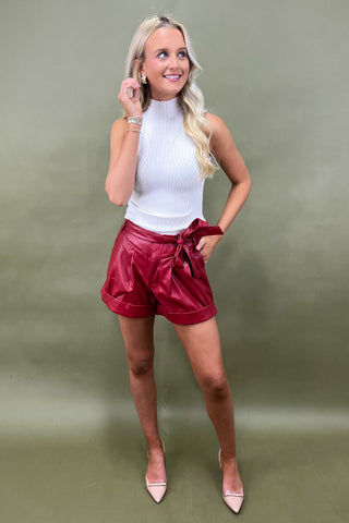 Woman wearing a white top and red leather shorts against a plain background