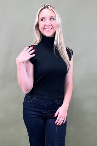 Woman wearing a black turtleneck and jeans against a plain background