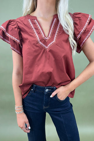 Woman wearing a burgundy blouse with ruffled sleeves and dark blue jeans on a plain background