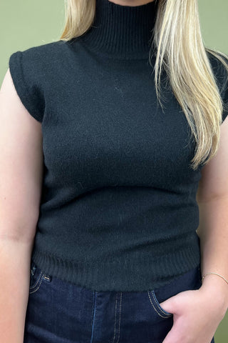 Person wearing a black sleeveless knit top against a green background