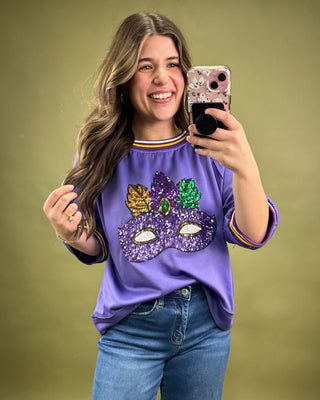 Woman taking a selfie wearing a purple shirt with a mask design on a green background