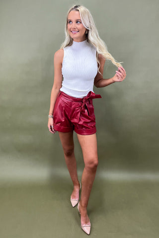 Woman wearing a white sleeveless top and red shorts against a green background