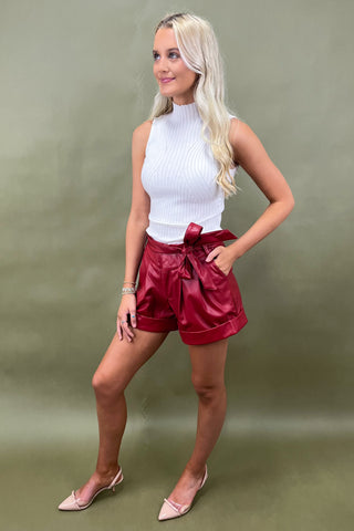 Woman wearing a white top and red shorts against a green background