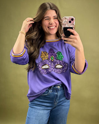 Woman taking a selfie wearing a purple shirt with a mask design on a green background