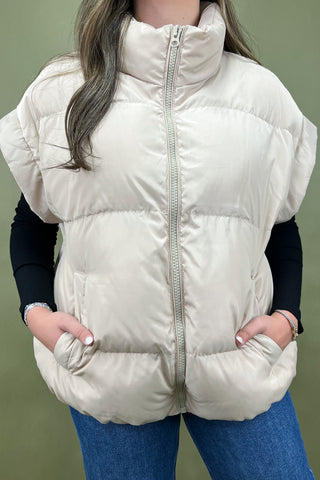 Person wearing a beige puffer vest against a green background