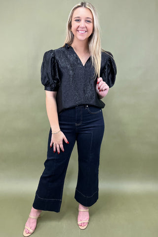 Woman wearing a black blouse and dark jeans against a green background
