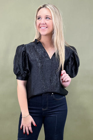 Woman wearing a black blouse with puffed sleeves against a green background