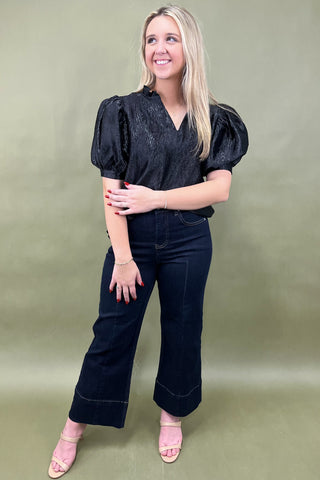 Woman wearing a black top and dark jeans against a green background