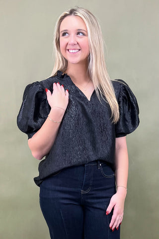 Woman wearing a black top with puff sleeves against a green background