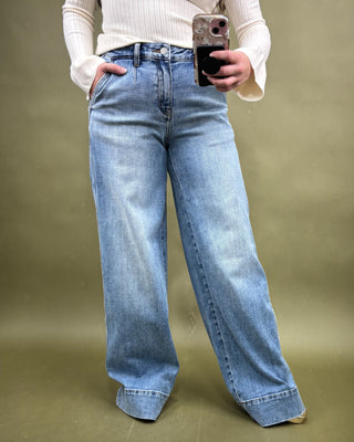 Person wearing light blue jeans and a white sweater against a green background