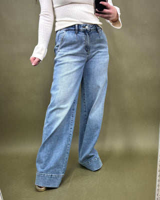 Person wearing blue jeans and a white sweater against a plain background