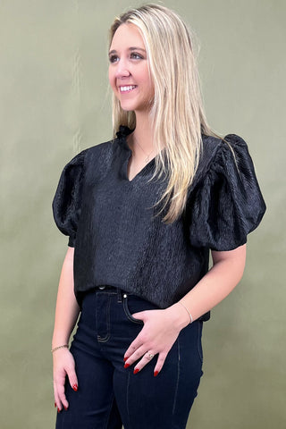 Woman wearing a black puff-sleeve top against a green background