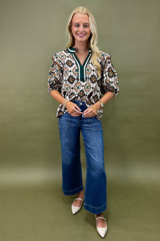 Woman wearing a patterned blouse and blue jeans against a green background
