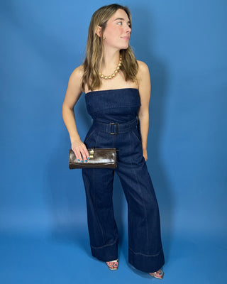 A woman modeling a dark blue denim strapless jumpsuit with wide legs and a matching belt