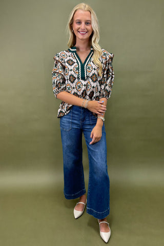 Woman wearing a patterned blouse and blue jeans against a green background