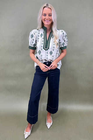 Woman wearing a patterned blouse and dark jeans against a plain background