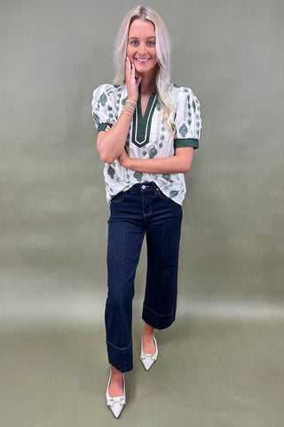 Woman wearing a patterned blouse and dark jeans against a plain background
