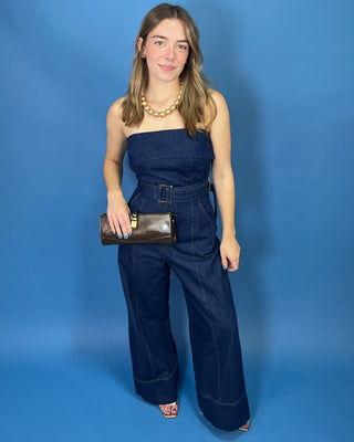 A woman modeling a dark blue denim strapless jumpsuit with wide legs and a matching belt