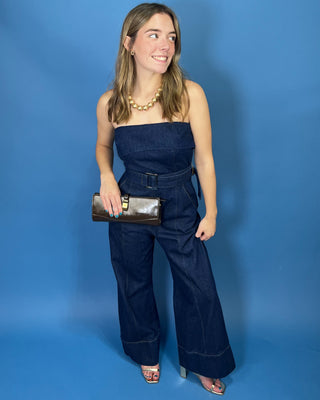 A woman modeling a dark blue denim strapless jumpsuit with wide legs and a matching belt