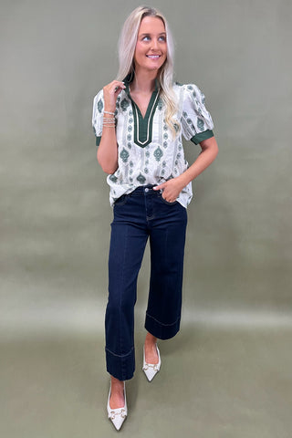 Woman wearing a patterned blouse and dark jeans against a neutral background