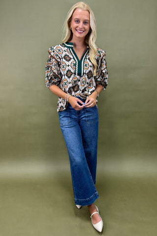 Woman wearing a patterned blouse and blue jeans against a green background