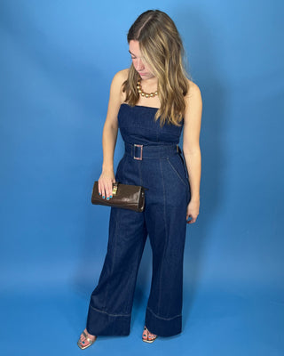 A woman modeling a dark blue denim strapless jumpsuit with wide legs and a matching belt