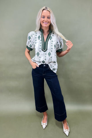 Woman wearing a patterned blouse and dark jeans against a plain background