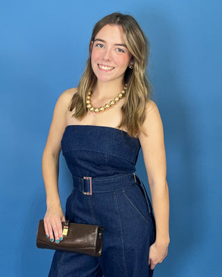 A woman modeling a dark blue denim strapless jumpsuit with wide legs and a matching belt