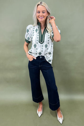 Woman wearing a patterned blouse and dark jeans against a plain background