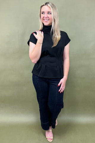 Woman wearing a black turtleneck top and black pants against a green background