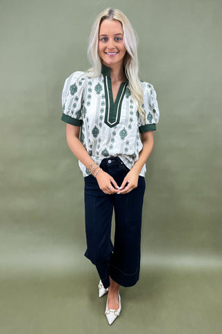 Woman wearing a patterned blouse and dark jeans against a plain background