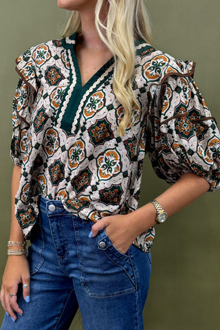 Woman wearing a patterned blouse and blue jeans against a green background