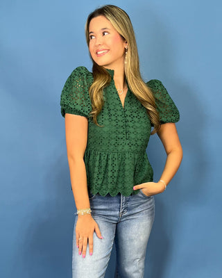 A woman modeling a dark green eyelet lace short-sleeve peplum top with light-wash blue jeans